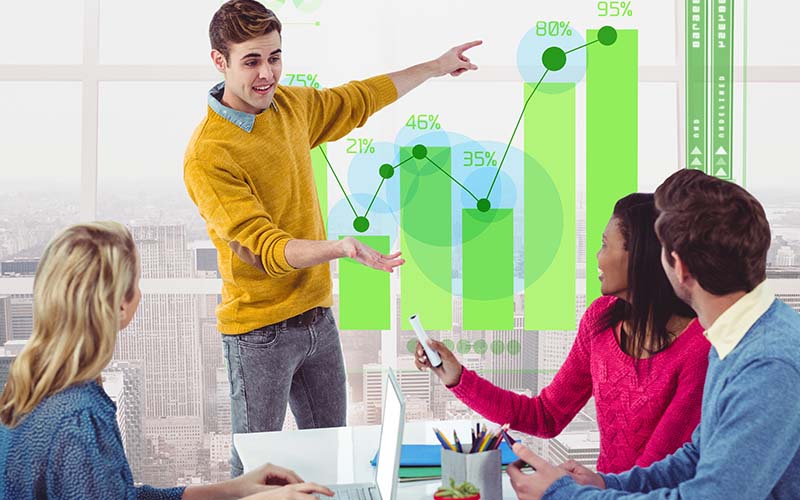 A diverse group of professionals discussing ideas in a meeting room, with a chart displayed on the wall.